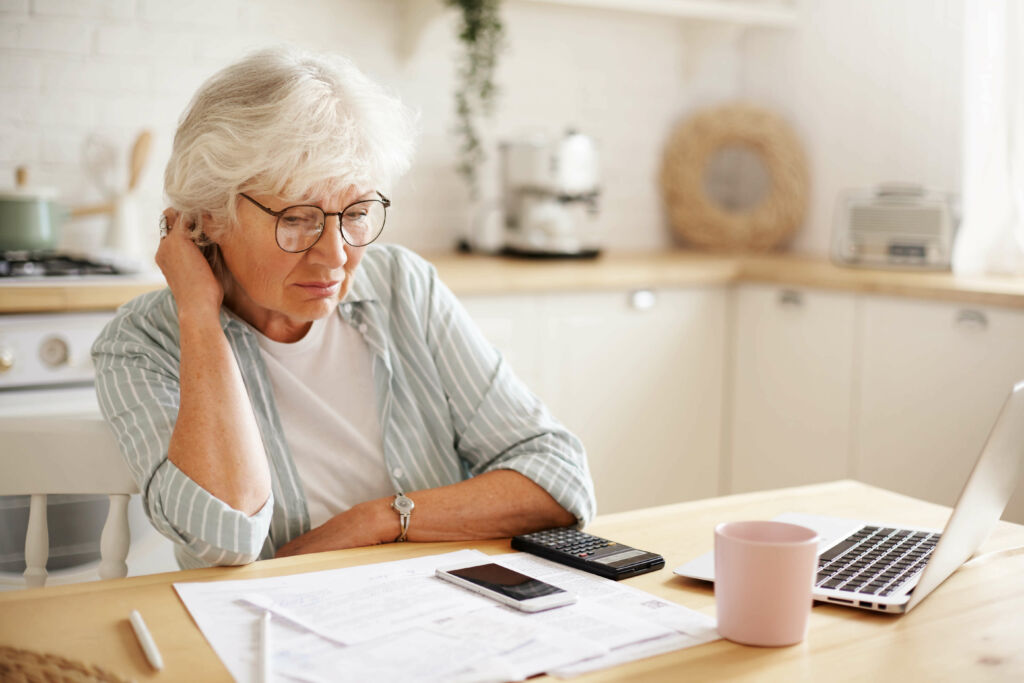 Older adult reviewing their finances on paper and on a laptop computer.