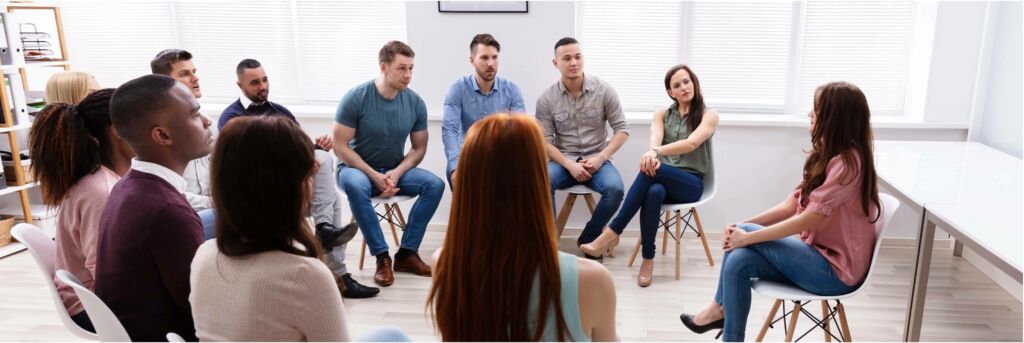 Group of people sitting on chairs in a circle representing a group counseling session.